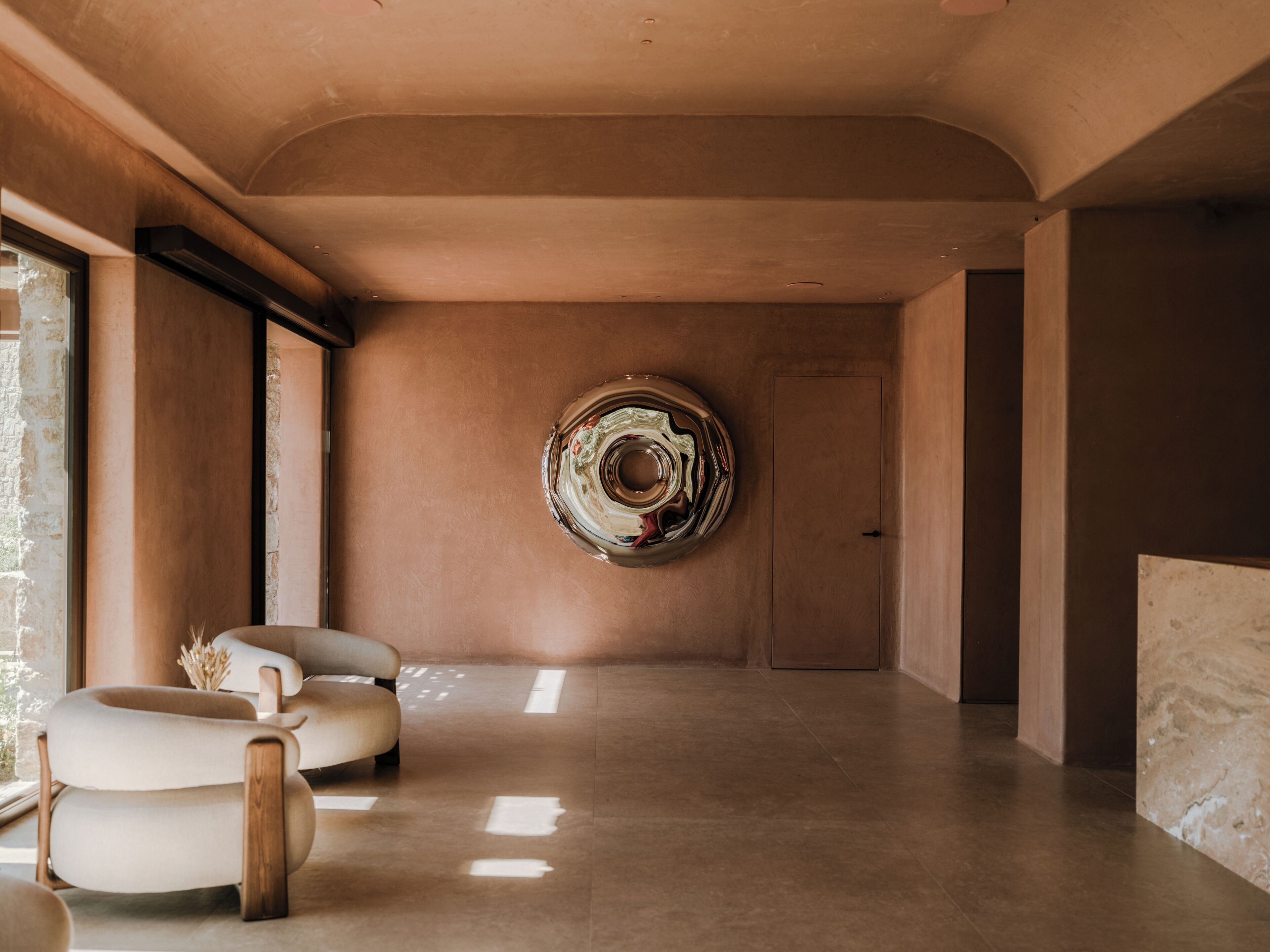 A spacious room with a modern design, featuring a large abstract artwork on the wall, a comfortable seating area with a sofa and chairs, and a large window providing natural light.