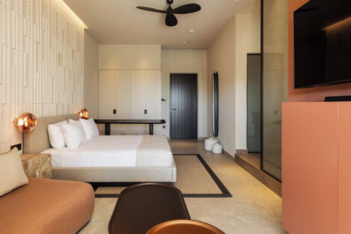 A modern hotel room with a bed, a sofa, a dining table, and a TV.