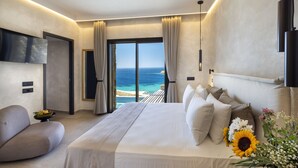 A modern hotel room with a large bed, a sofa, a flat-screen TV, and a view of the ocean. - Tropicana Suites & Villas (Mykonos)