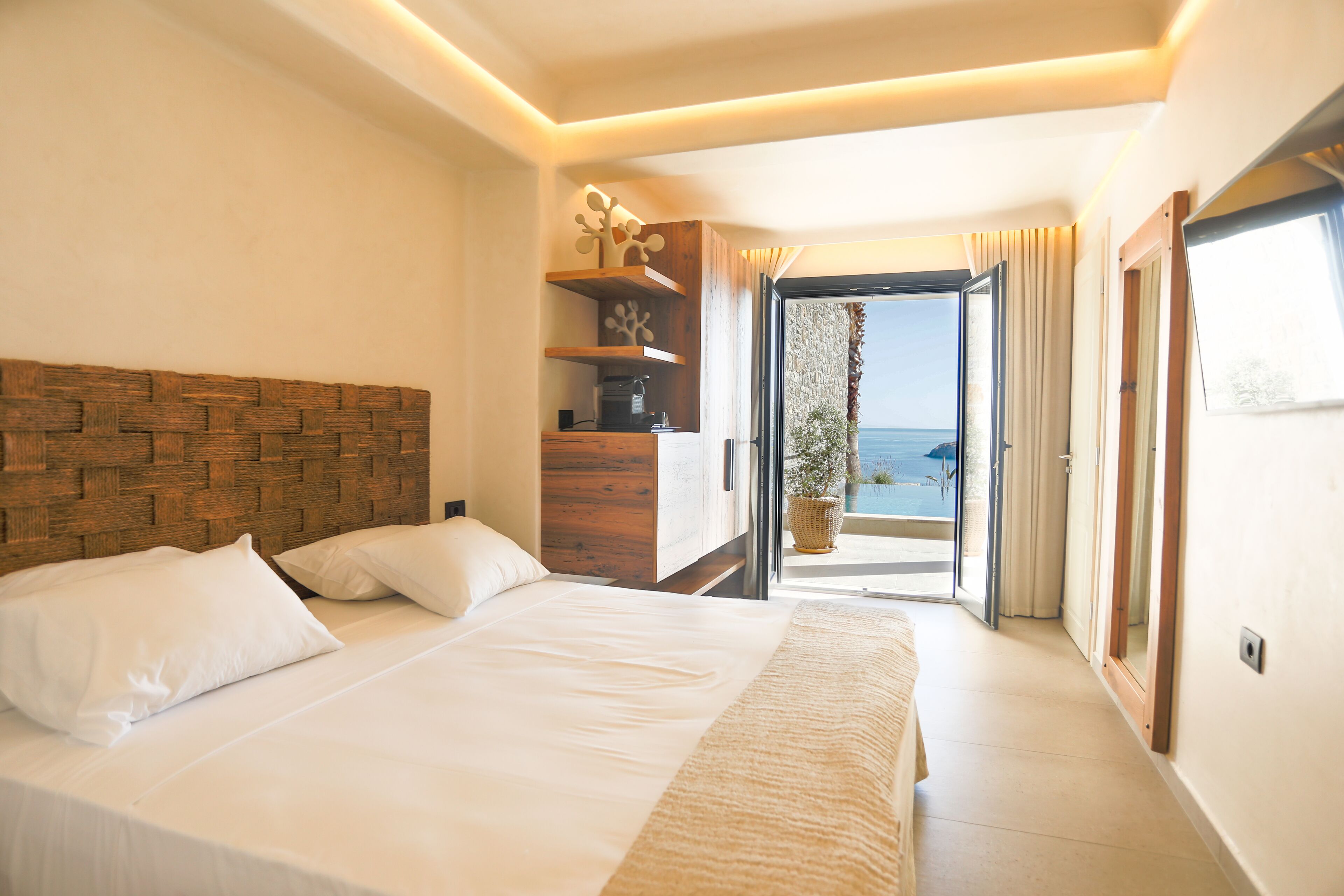 Una habitación de hotel moderna con una cama grande, cabecera de madera, estante empotrado y balcón con vista al mar.