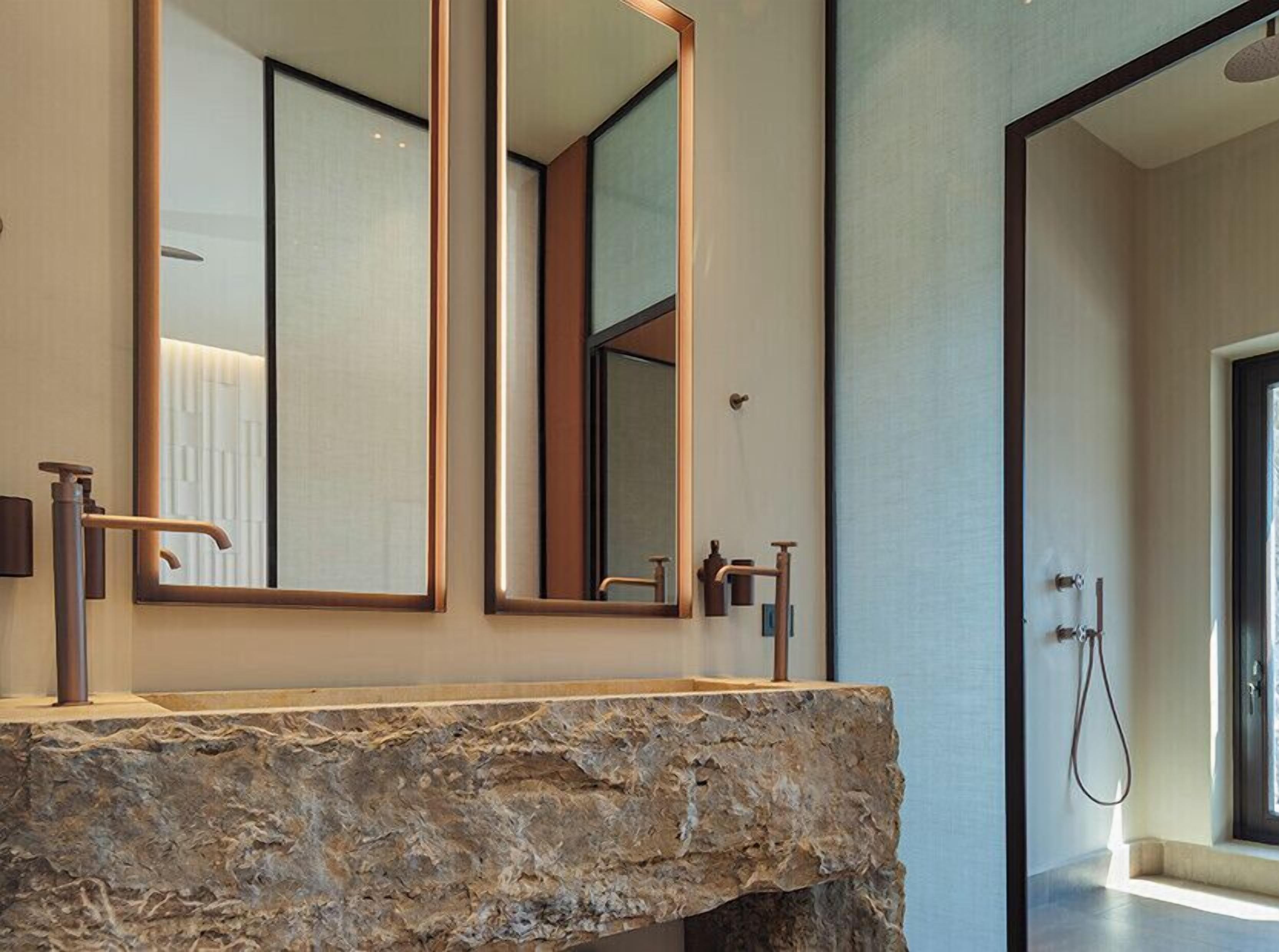 A bathroom with a stone countertop, a large mirror, and a shower area.