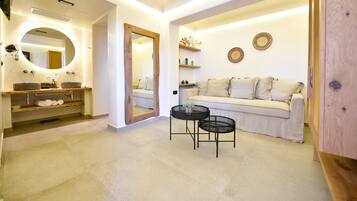 Un baño moderno con tocador, espejo y repisas. En la zona de estar contigua hay un sofá y una mesita.