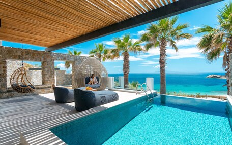 A pool area with a view of the sea, stone walls, and a hanging chair.