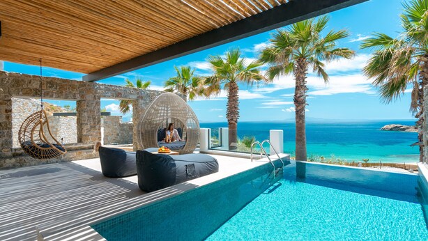 A pool area with a view of the sea, stone walls, and a hanging chair. - Tropicana Suites & Villas (Mykonos)