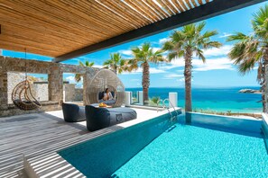 Zona de piscina con vista al mar, muros de piedra y una silla colgante.
