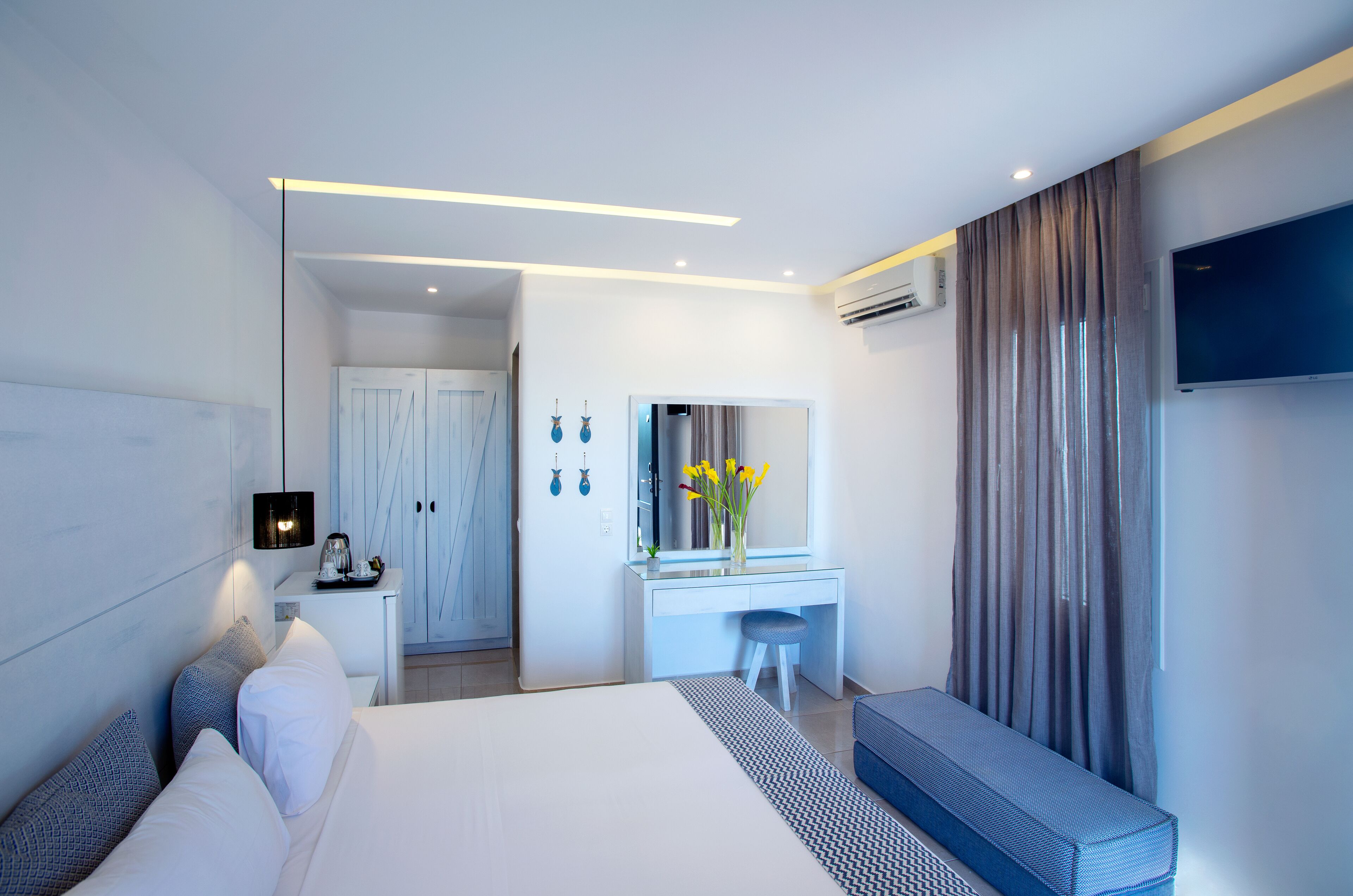 A modern hotel room with a large bed, a desk with a mirror, a TV, and a seating area.