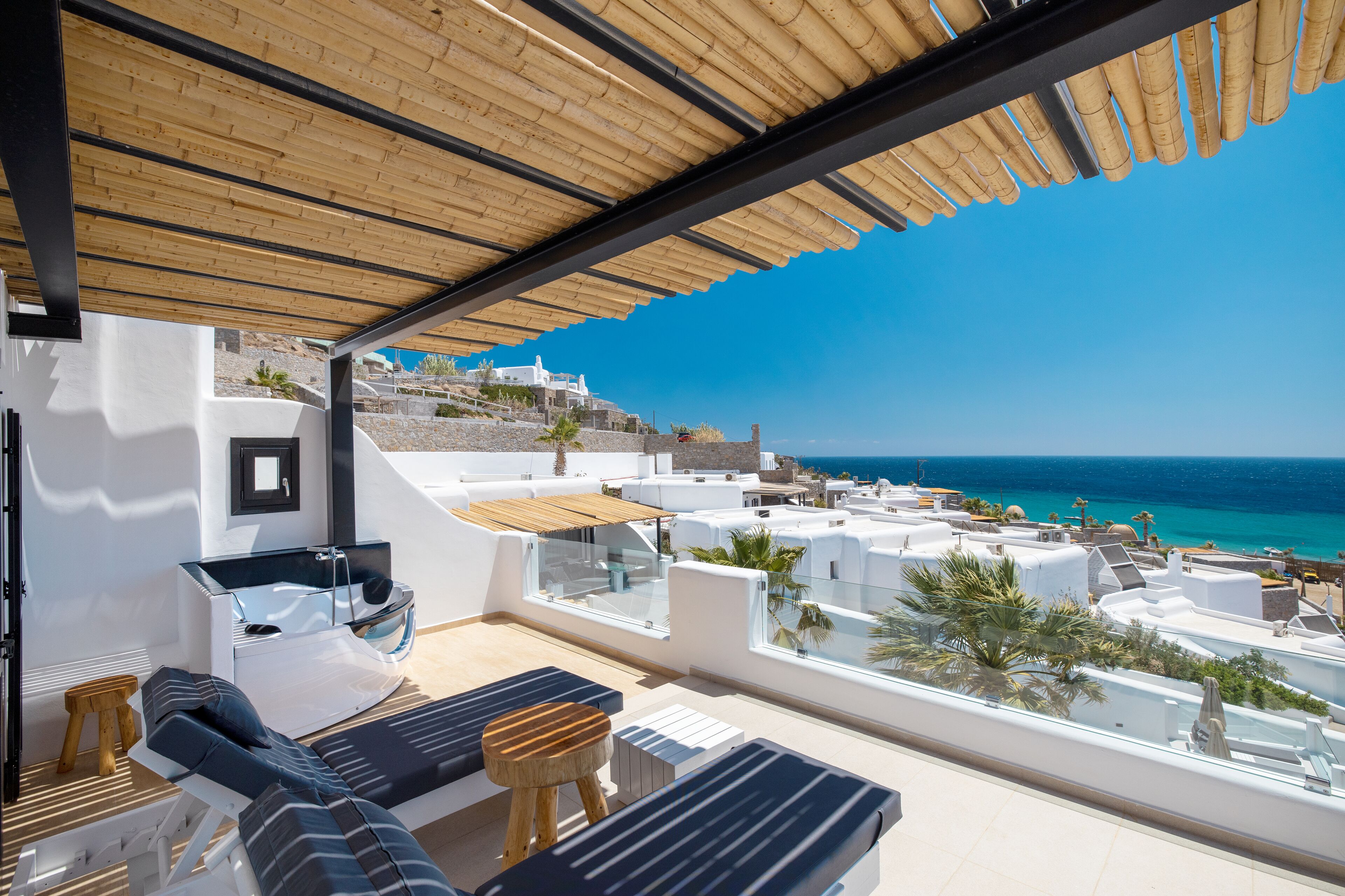 A rooftop terrace with lounge chairs, a glass-enclosed jacuzzi, and a view of the coastline.