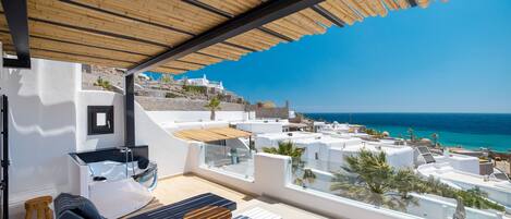 A rooftop terrace with lounge chairs, a glass-enclosed jacuzzi, and a view of the coastline.