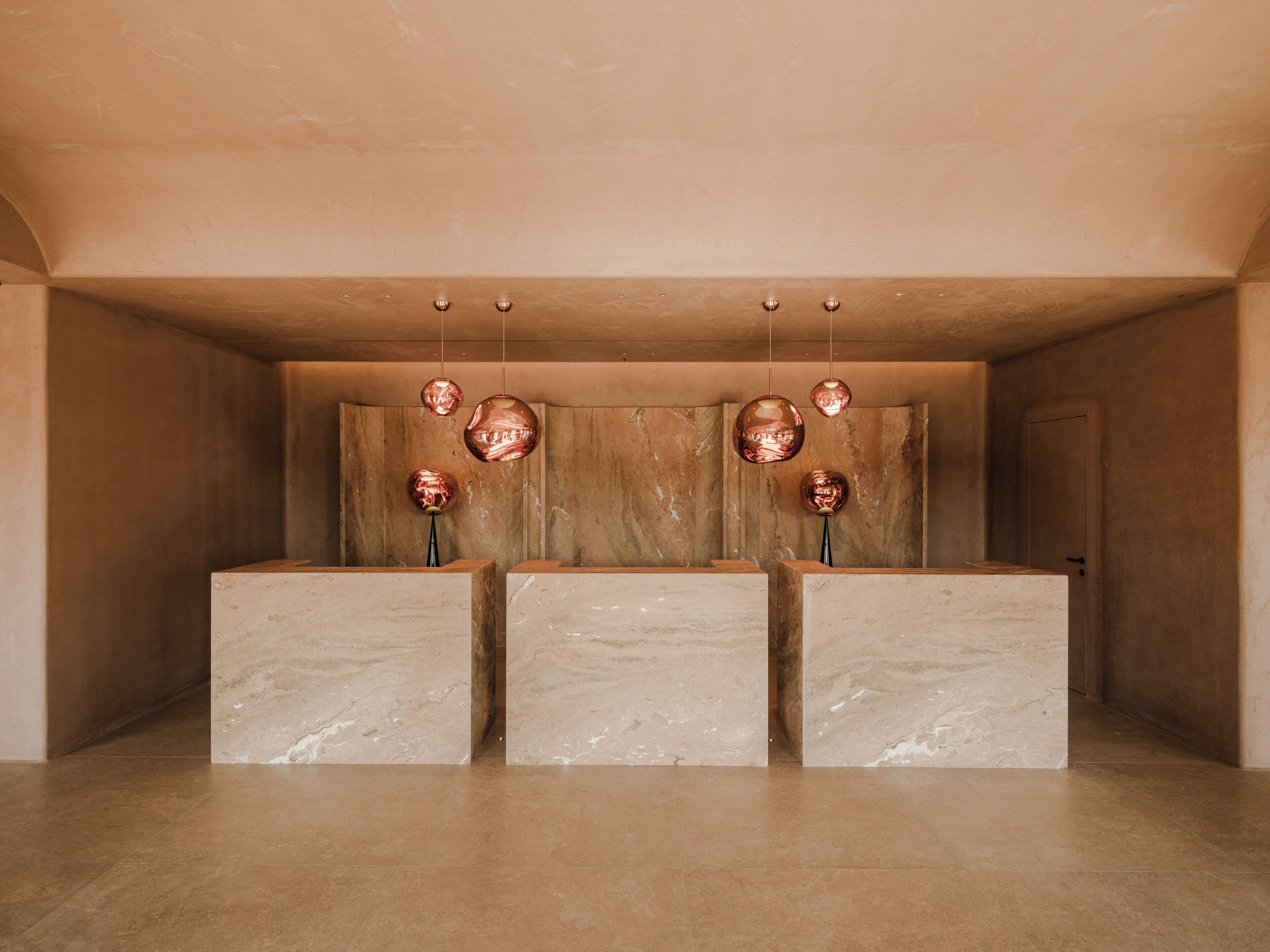 A reception area with marble counters and copper spherical pendant lights.