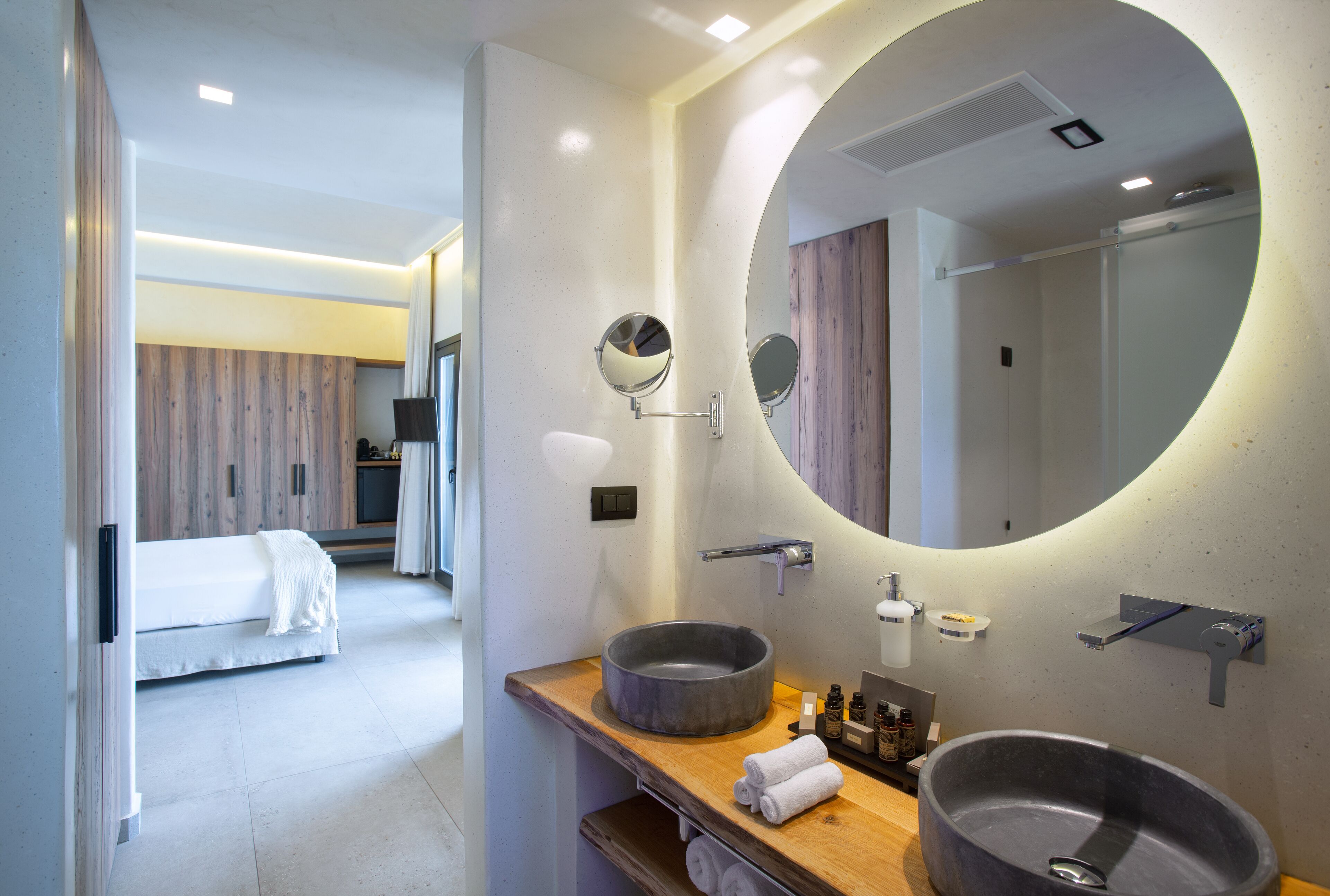 A modern bathroom with a round mirror, a round sink, and a wooden vanity.
