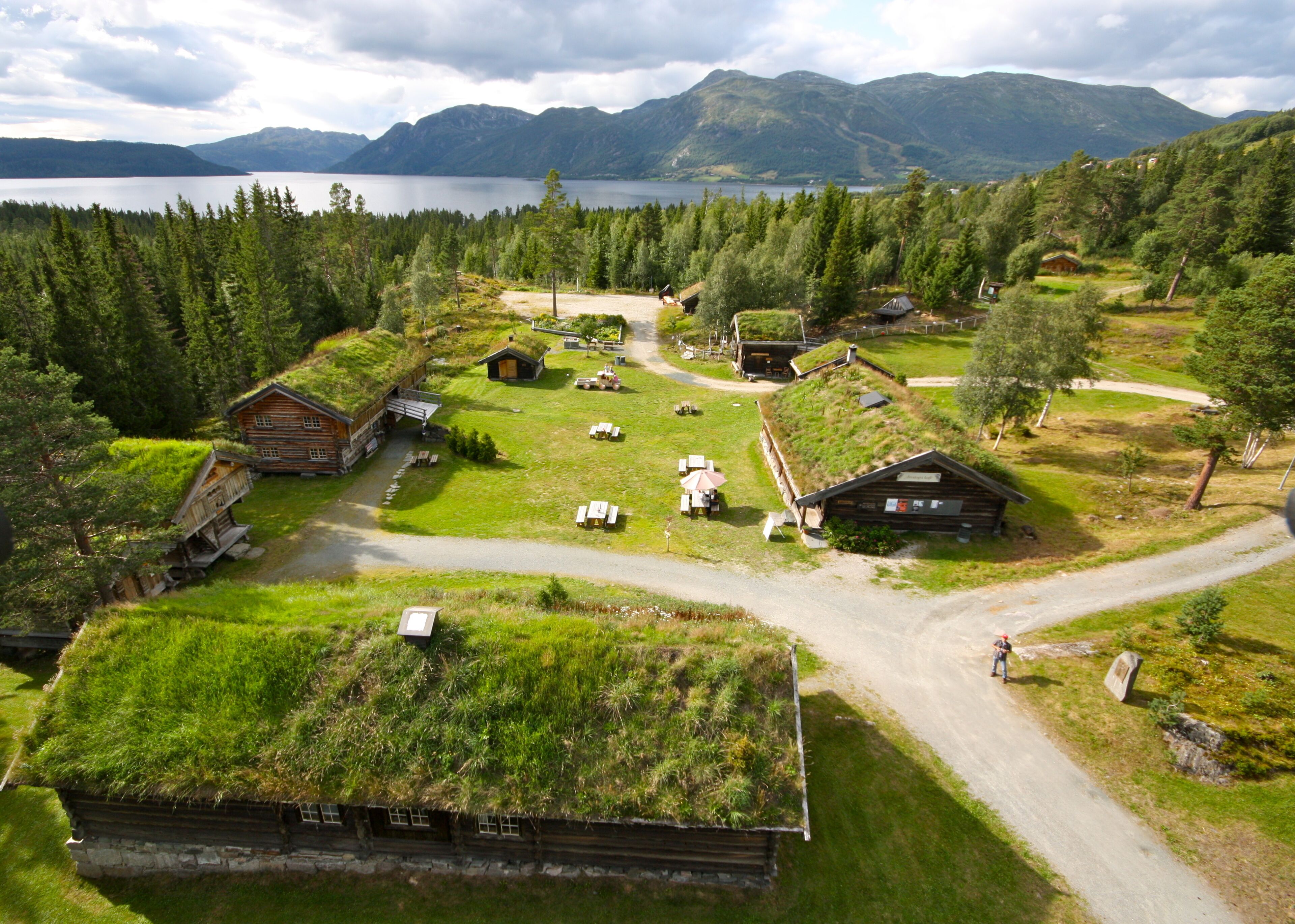 A remote village with traditional grass-roofed houses, a clear road, and a lake in the background.