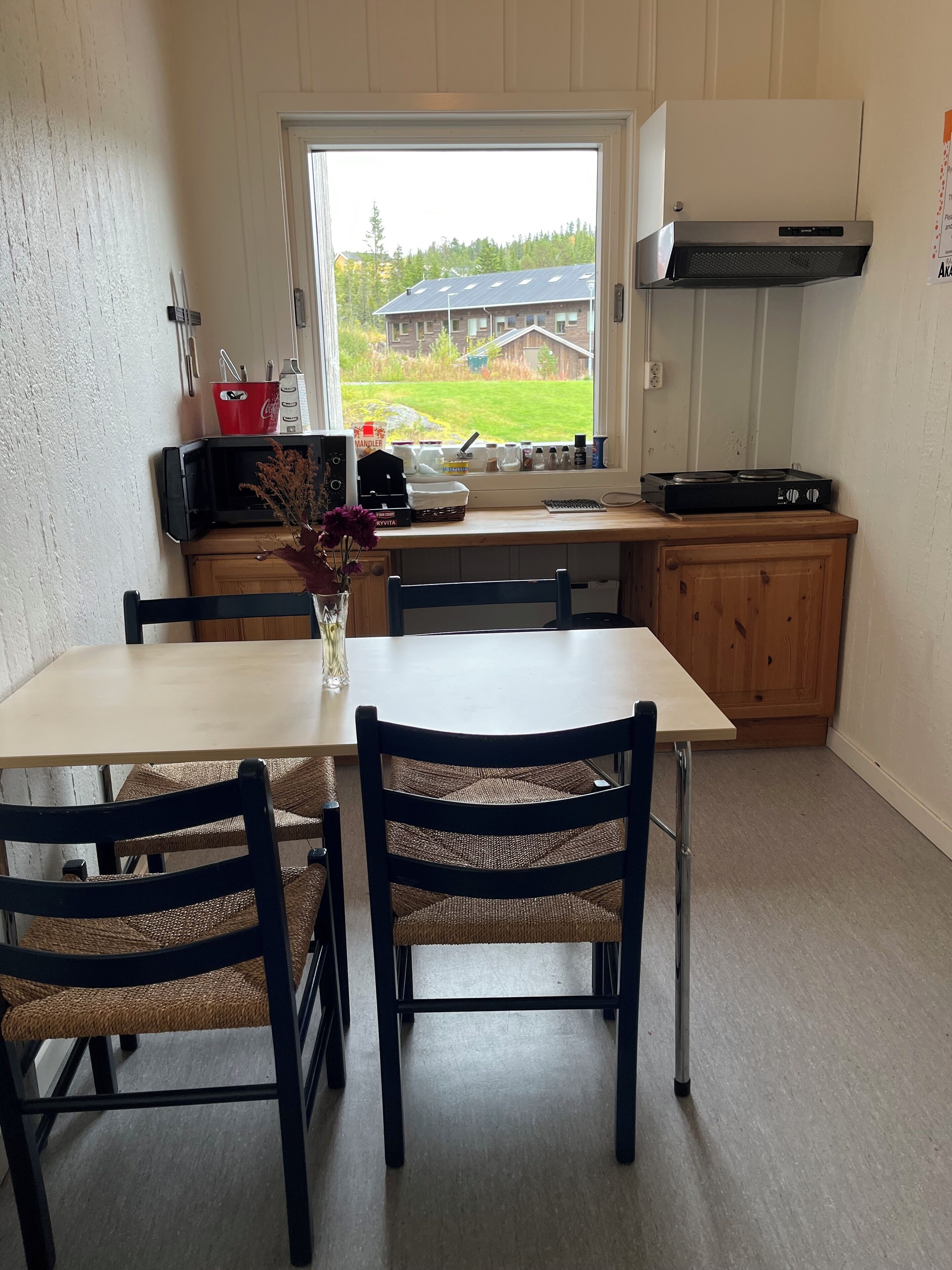 A kitchen with a dining table, chairs, a window with a view of a house and trees, a microwave, a gas stove, and a cabinet.