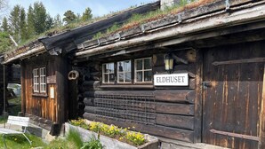 Une cabane rustique en rondins de bois, sur laquelle est apposée une enseigne indiquant « ELDHUSET ».