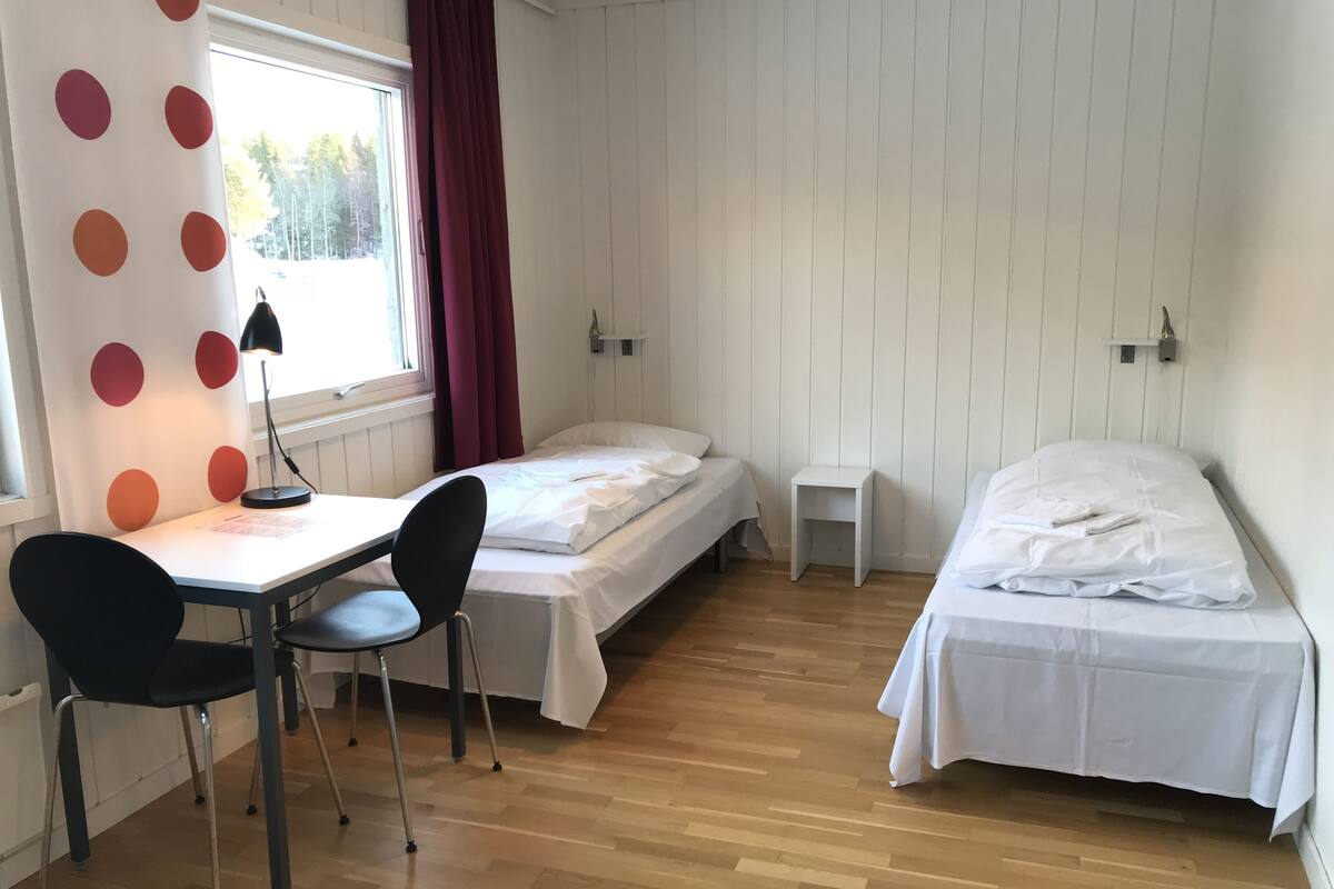 A room with two beds, a desk with a chair, and a window with curtains.
