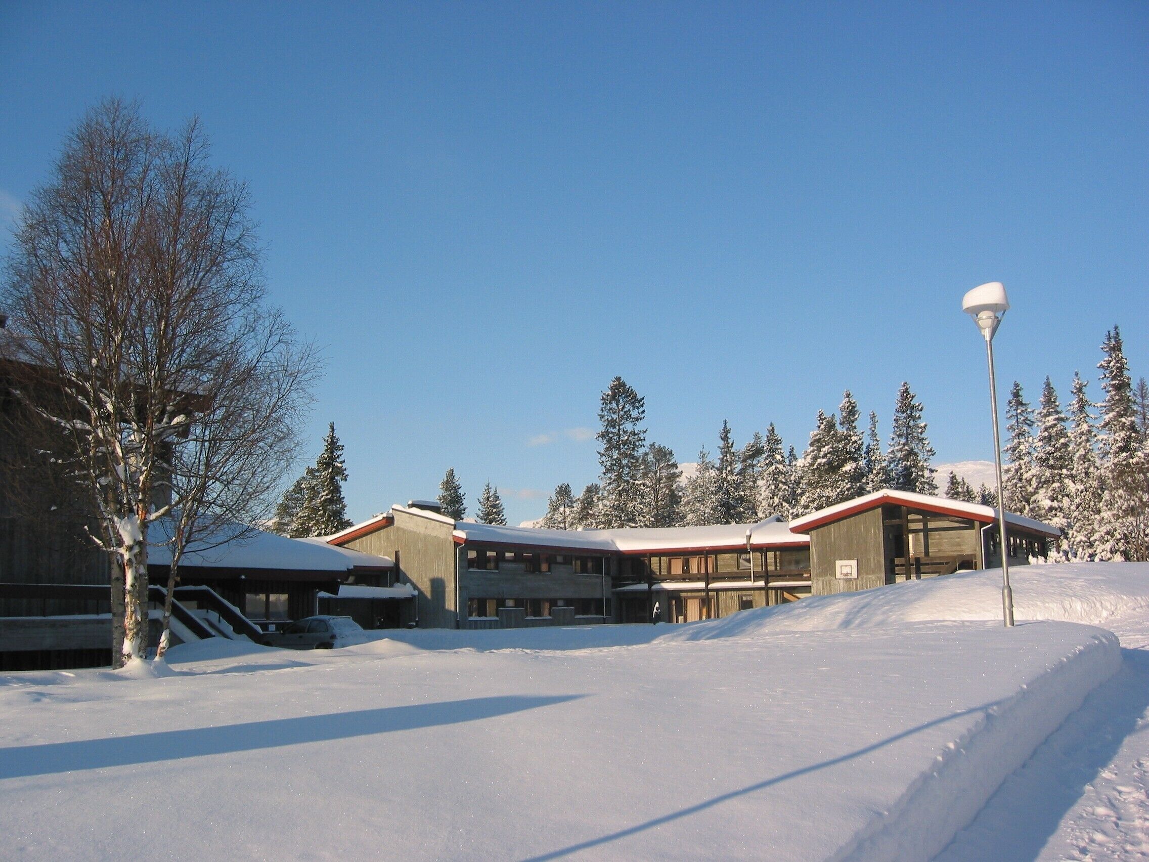 A snow-covered building with a red roof, surrounded by trees and a clear sky.