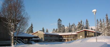 A snow-covered building with a red roof, surrounded by trees and a clear sky.
