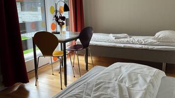A hotel room with two beds, a desk with a chair, a window with curtains, and a view of the outside.