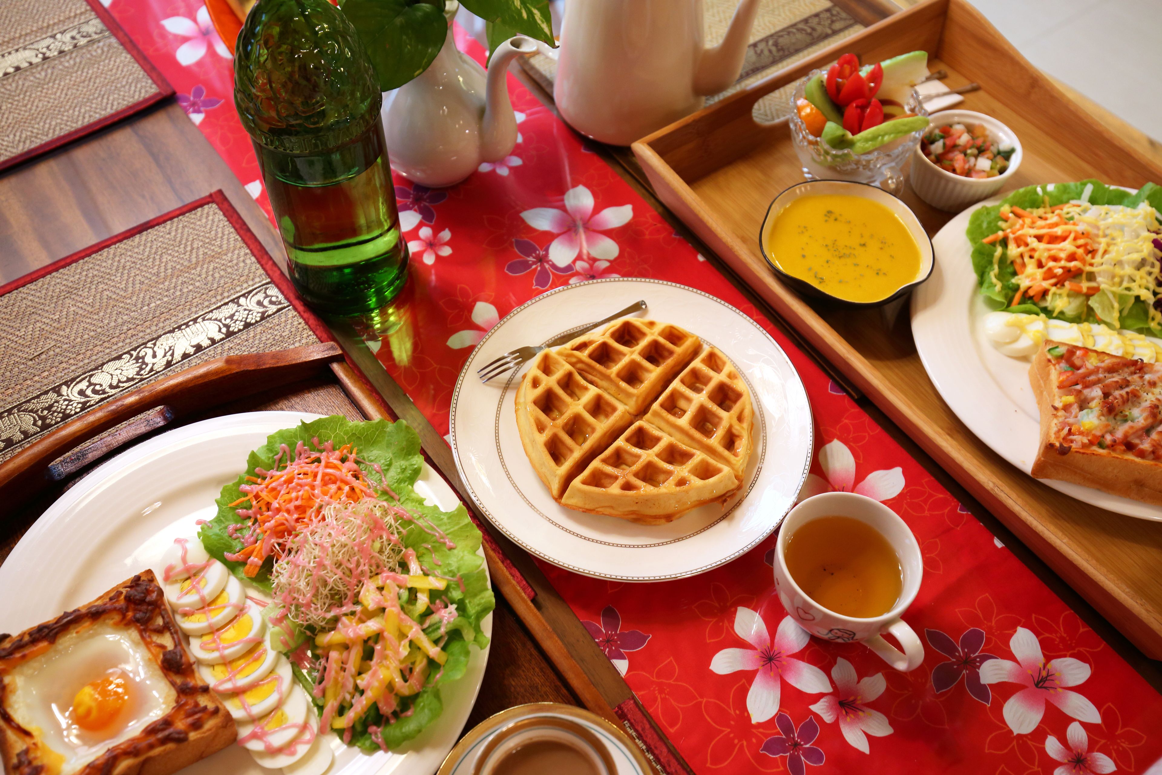 Een dienblad met wafels, salade, eieren en een kop thee.