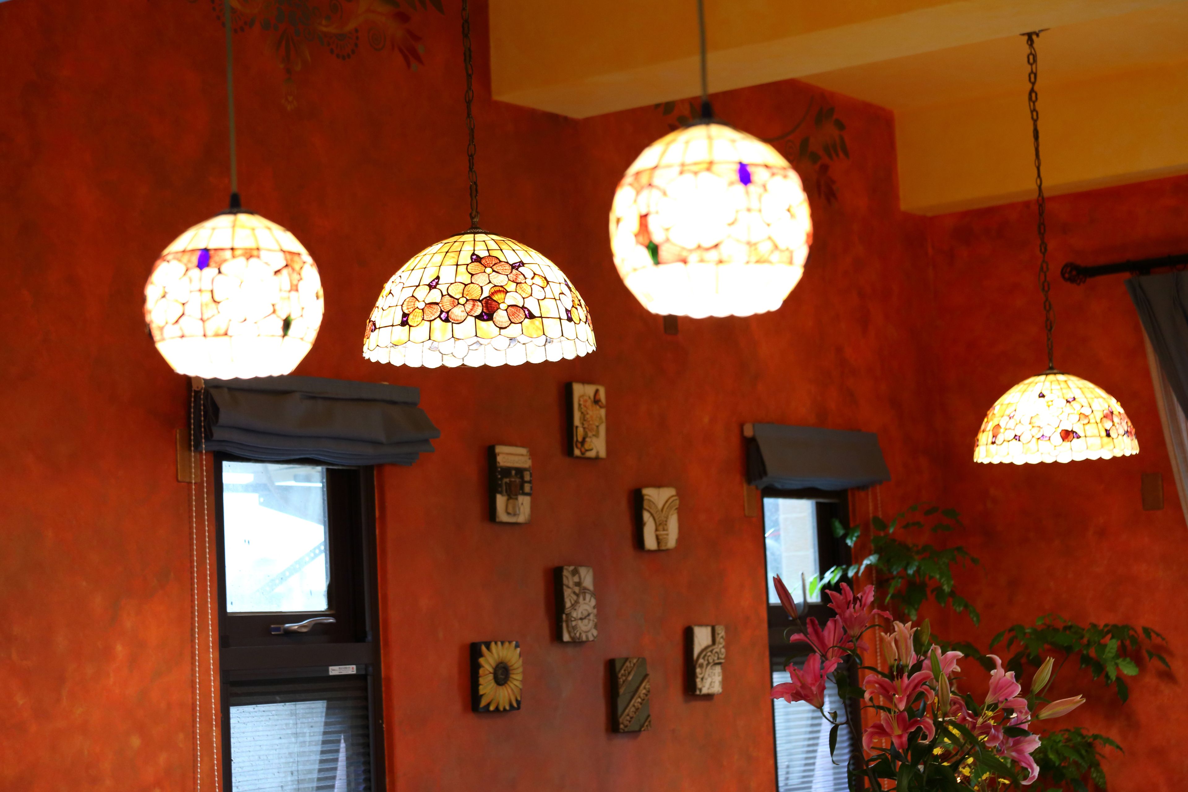 A room with three hanging glass lamps, a window with blinds, and a wall decorated with various small artworks.
