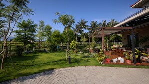 Un jardin agrémenté d’une terrasse dallée, d’une pergola et de coins salon extérieurs.