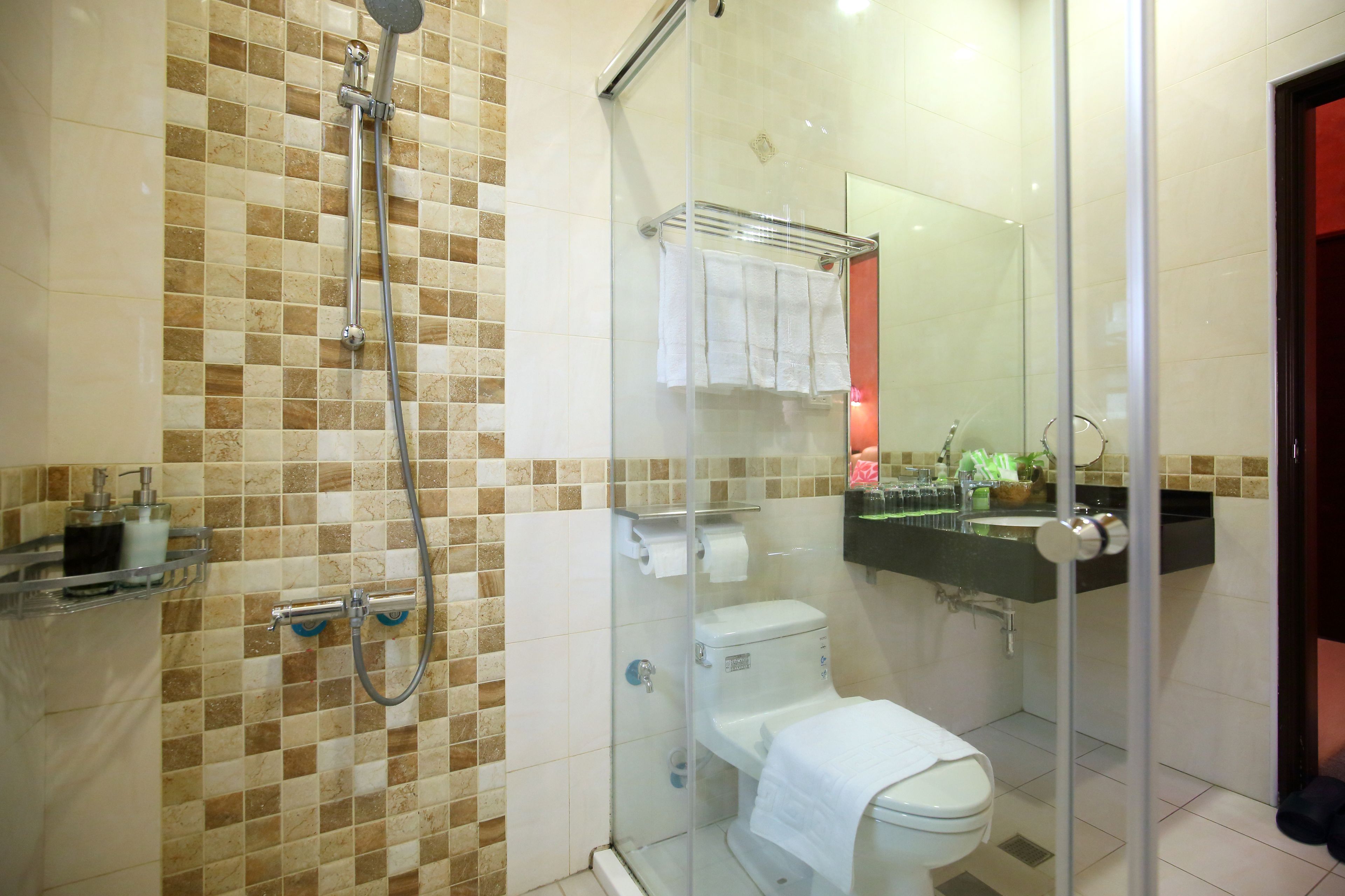 A bathroom with a glass-enclosed shower, a toilet, and a sink with a mirror above it.