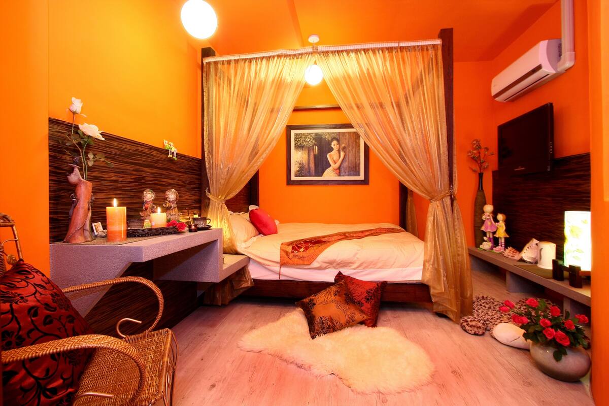 A room with a bed, a vanity with candles, a chair, and a vase with flowers.