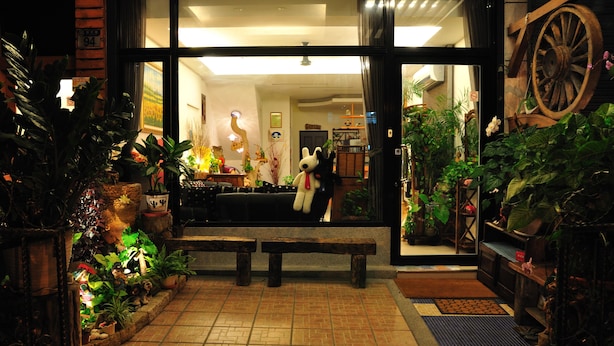A well-lit entrance with a large window, a wooden bench, and various potted plants. - Sweet Heart Hostel (Hualien City)
