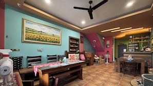 A room with a ceiling fan, a painting of sunflowers, a wooden bench, a table with a red tablecloth, and a bar area with shelves. - Sweet Heart Hostel (Hualien City)