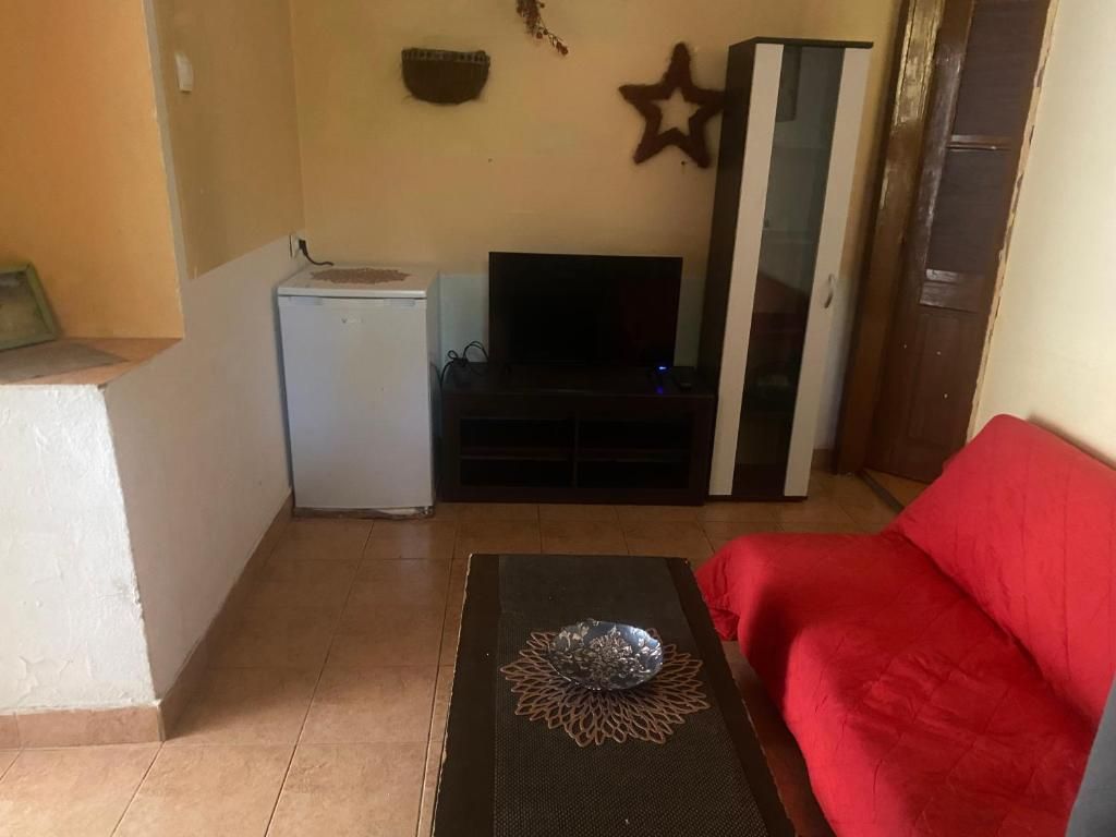 Una sala de estar con un sofá rojo, un televisor, un mueble blanco pequeño y una estrella decorativa en la pared.
