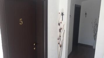 A dark wooden door with the number 5, a white wall with a decorative plant, and an archway leading to a dark interior.
