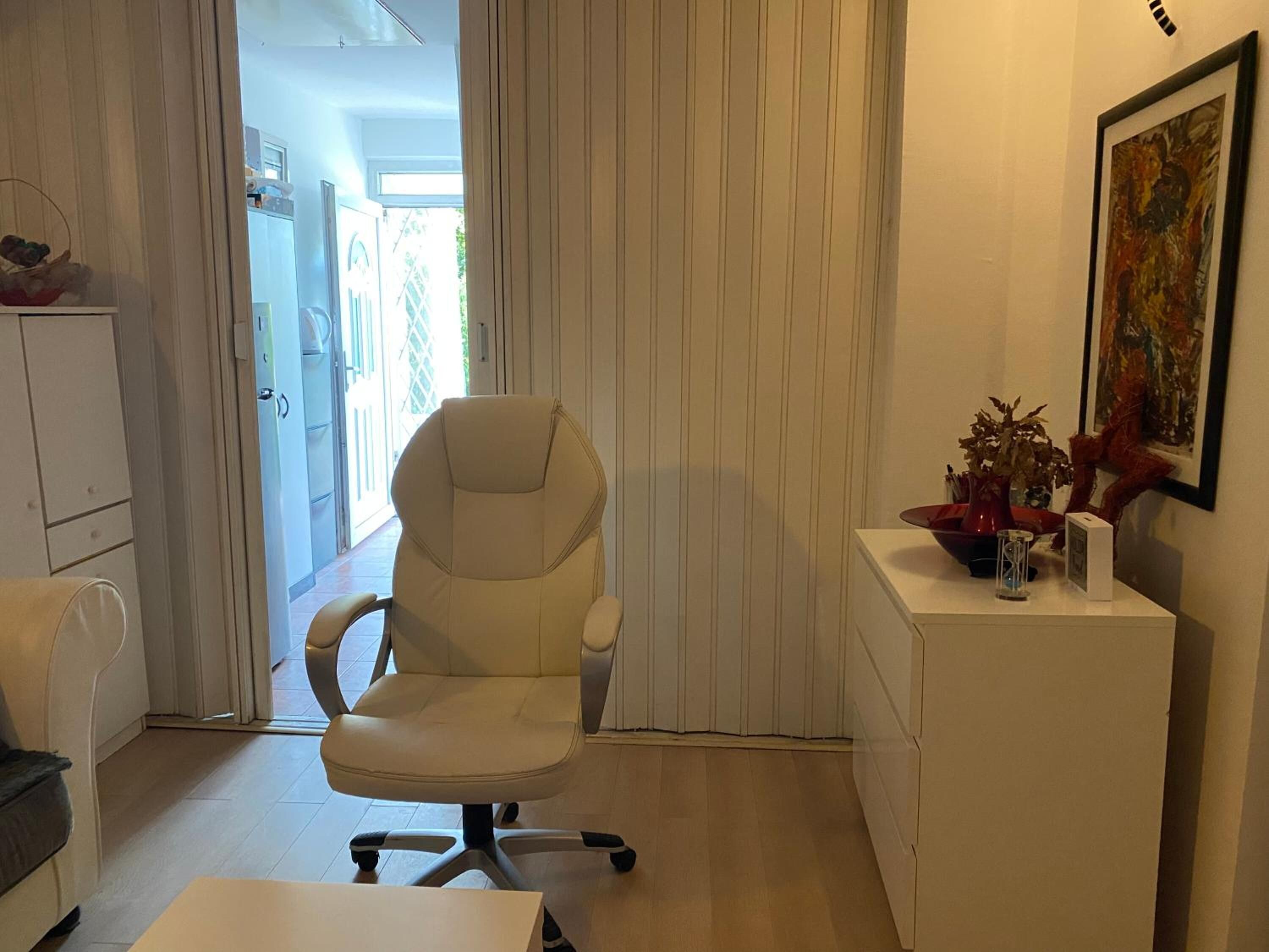 A modern office space with a white office chair, a desk, and a small side table with decorative items.