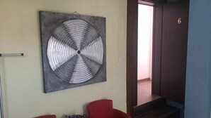 Una habitación con una gran obra de arte abstracta en la pared, dos sillones rojos, una mesa pequeña con una cesta y una escalera que conduce a otra habitación.