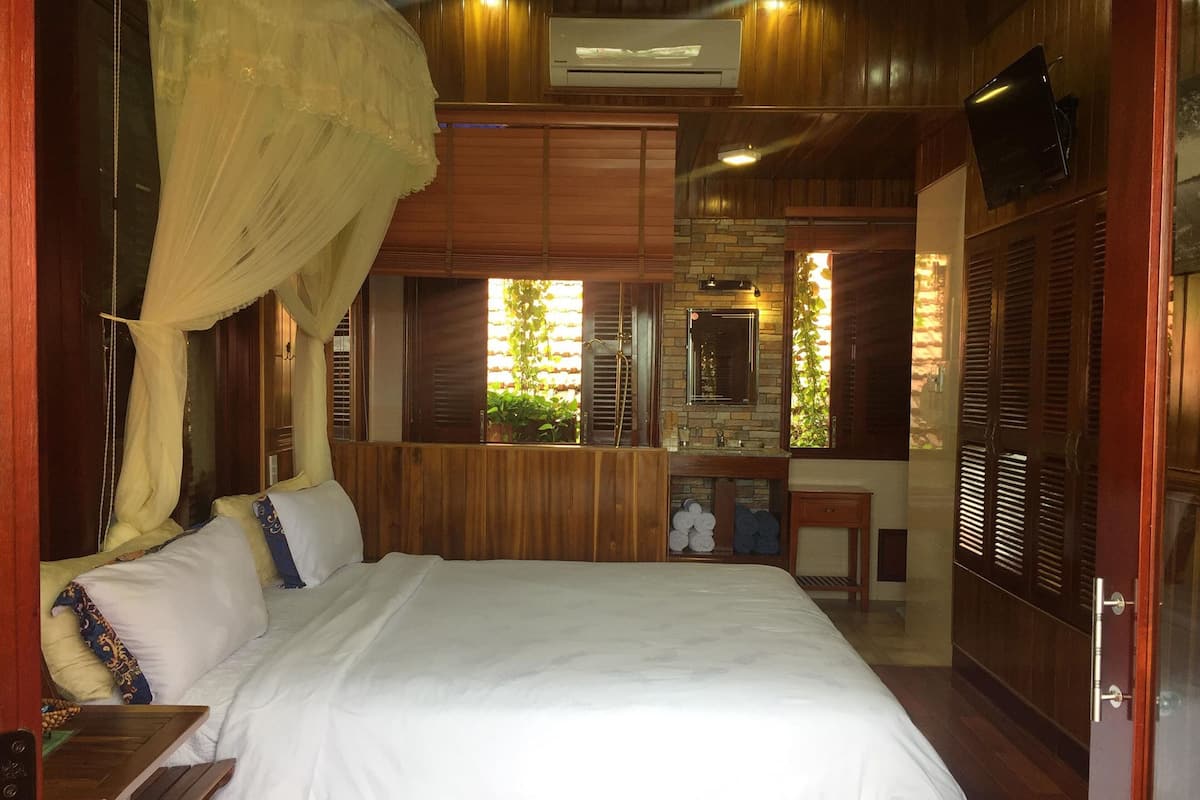 Un dormitorio con una cama, cabecera de madera, tocador con espejo y televisión montada en la pared.