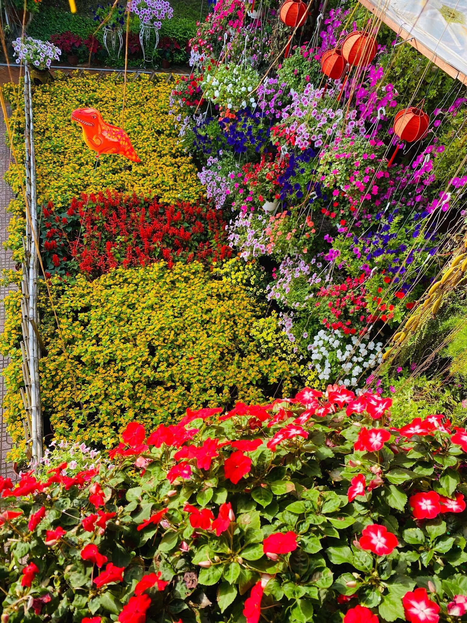 A garden with various colorful flowers and a large red dinosaur decoration.