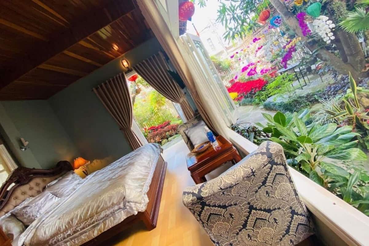 Una habitación con una cama, un sofá y vistas a un jardín con diversas plantas y flores.