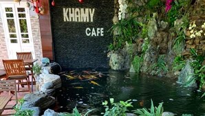 A wooden table surrounded by fruit-shaped stools in a cafe setting with a koi pond and greenery. - Khamy Riverside Resort (Da Nang)