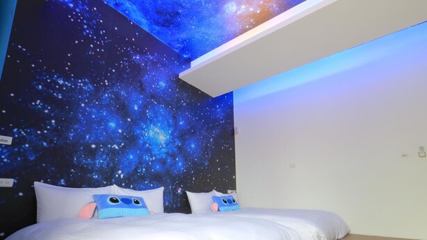 Une chambre avec un décor mural sur le thème de la galaxie, deux lits avec du linge de lit blanc et un plancher en bois.