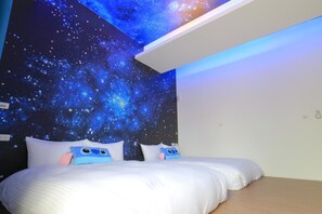 Ein Schlafzimmer mit Wandgemälde zum Thema Galaxie, zwei Betten mit weißer Bettwäsche und Holzboden.