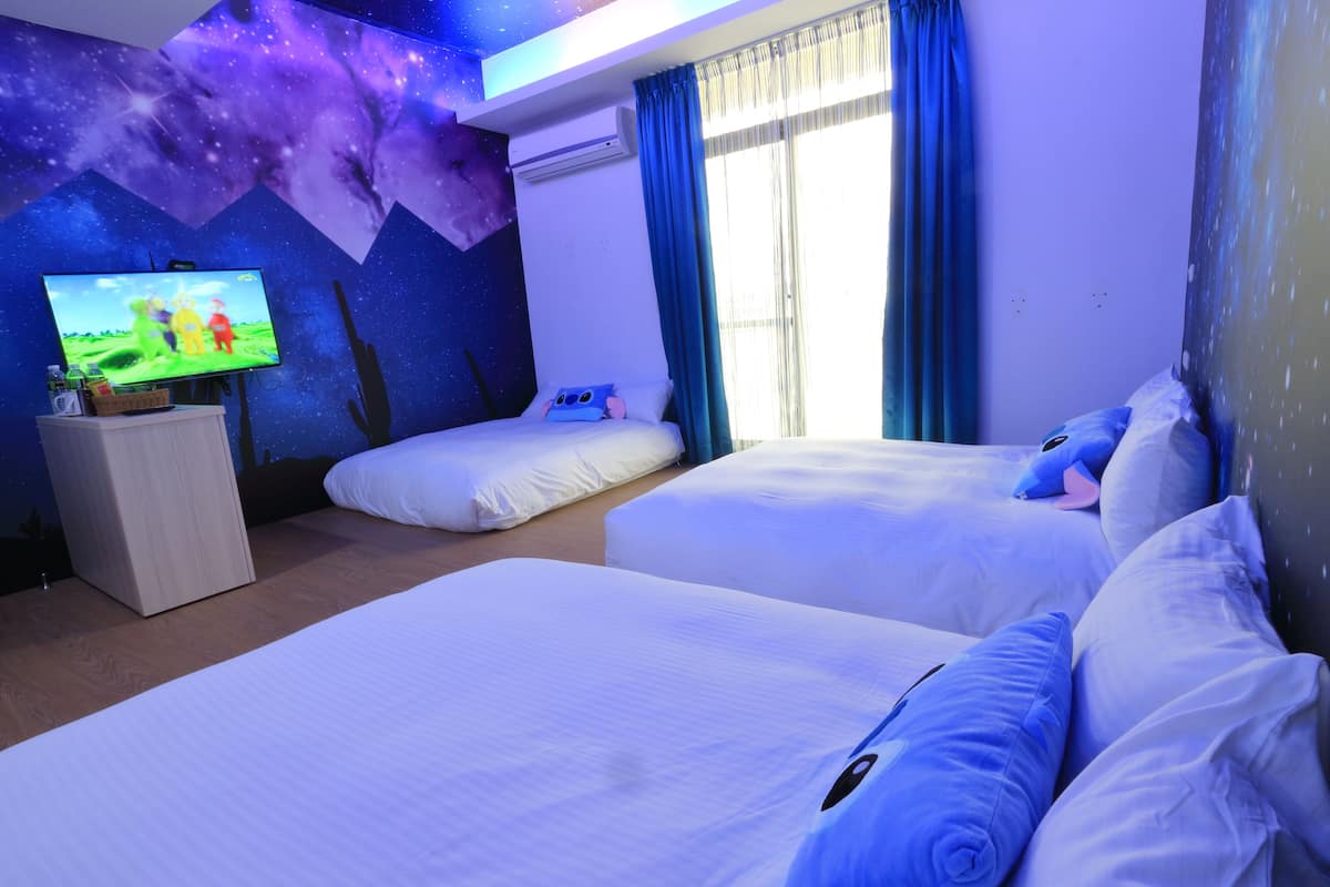 Habitación de hotel con dos camas, un televisor de pantalla plana, un mural en la pared y una ventana con cortinas.