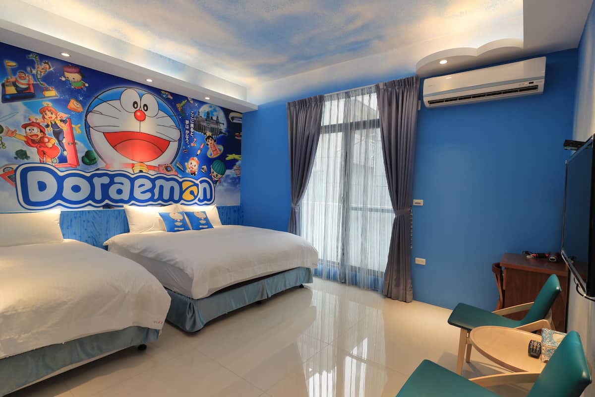 Habitación de hotel con dos camas, un gran mural de Doraemon, un televisor y una ventana con cortinas.