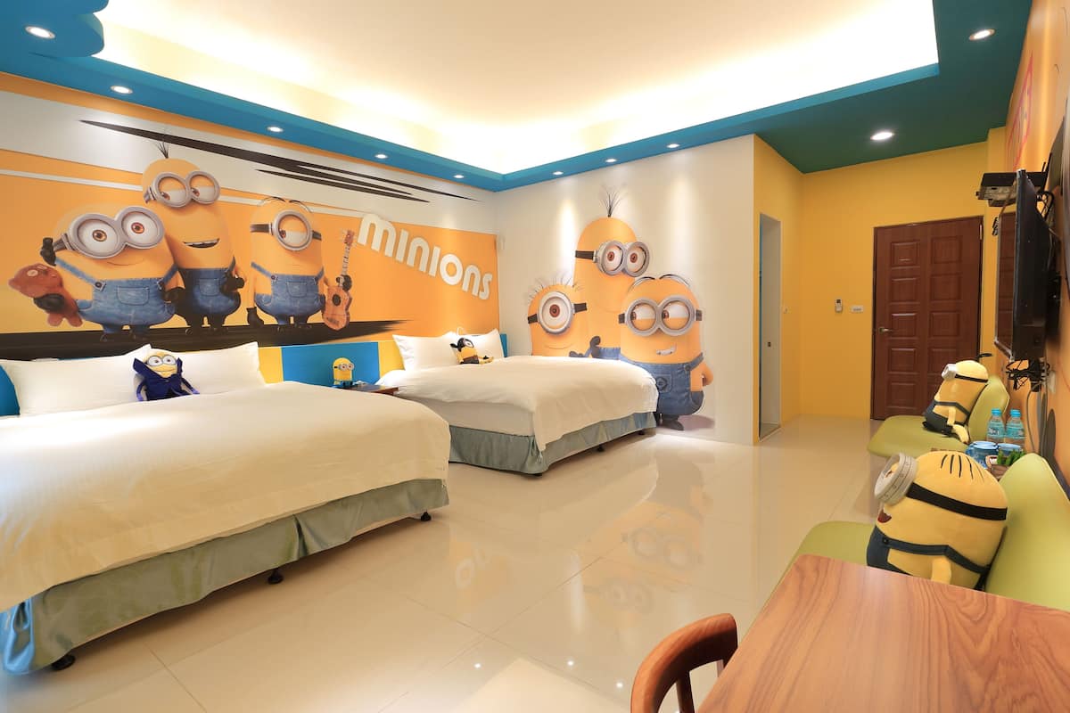 Habitación de hotel con dos camas, una mesa de comedor y una pared decorada con personajes de Minions.