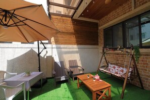 An outdoor patio with a wooden table, chairs, a swing, and a large umbrella. - Sunshine B&B (Hualien City)