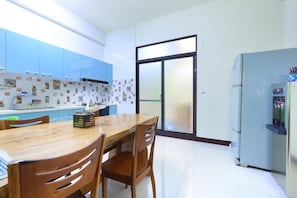A modern kitchen with a wooden dining table, chairs, a refrigerator, and a sliding glass door. - Sunshine B&B (Hualien City)