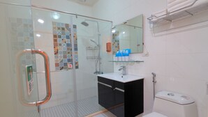 Une salle de bain moderne avec une douche à l’italienne en verre, un meuble-lavabo noir avec un vasque blanche et des toilettes blanches.