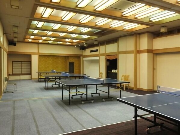 Una sala con varias mesas de ping pong, piso alfombrado e iluminación lineal en el techo.