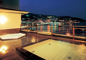 A rooftop pool with a glass balustrade, a hot tub, and a cityscape view at dusk. - Uomisaki Hotel (Atami)