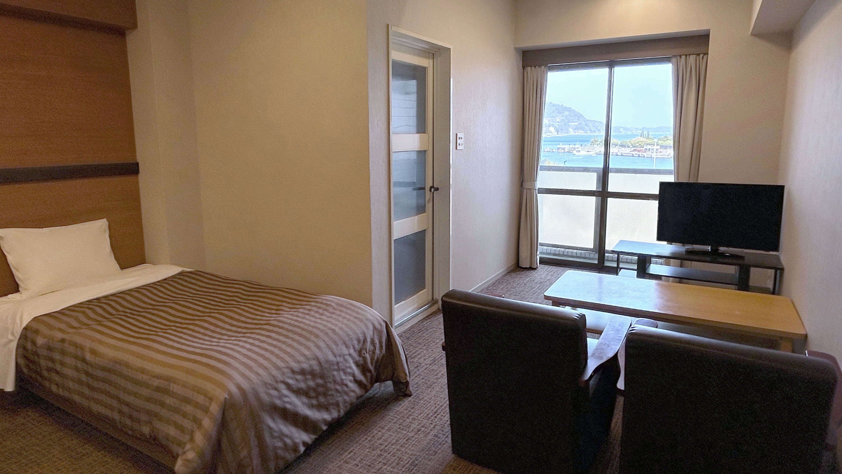 Una habitación de hotel con una cama, un escritorio con televisor y vistas al mar.