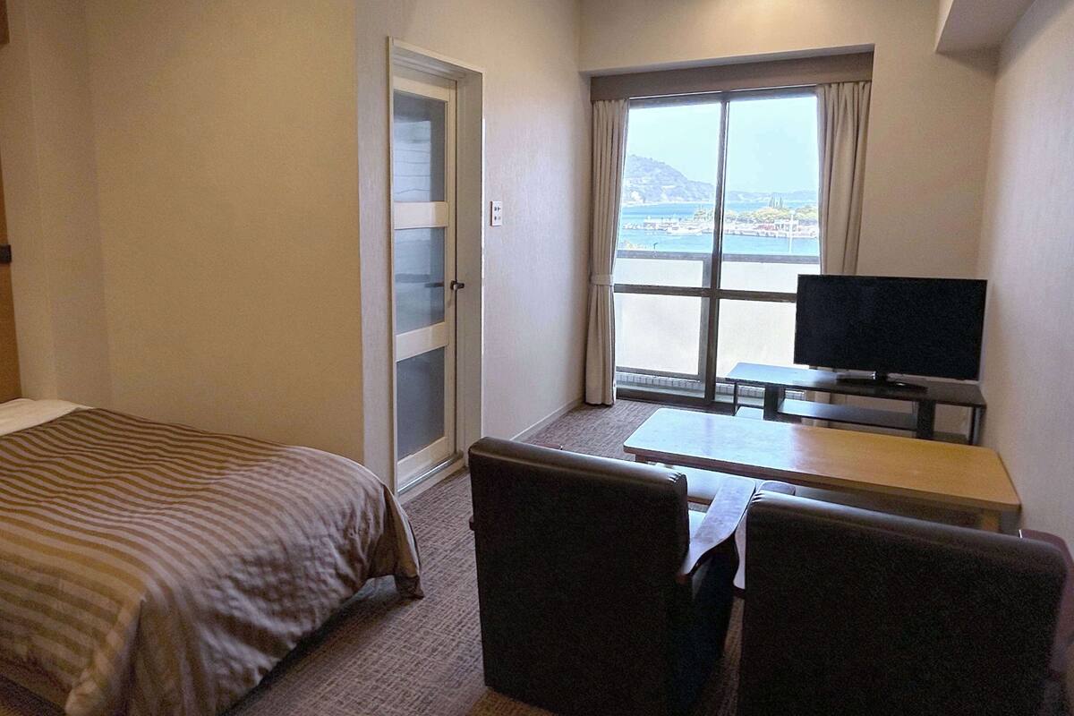 Una habitación de hotel con una cama, un escritorio con televisor y vistas al mar.