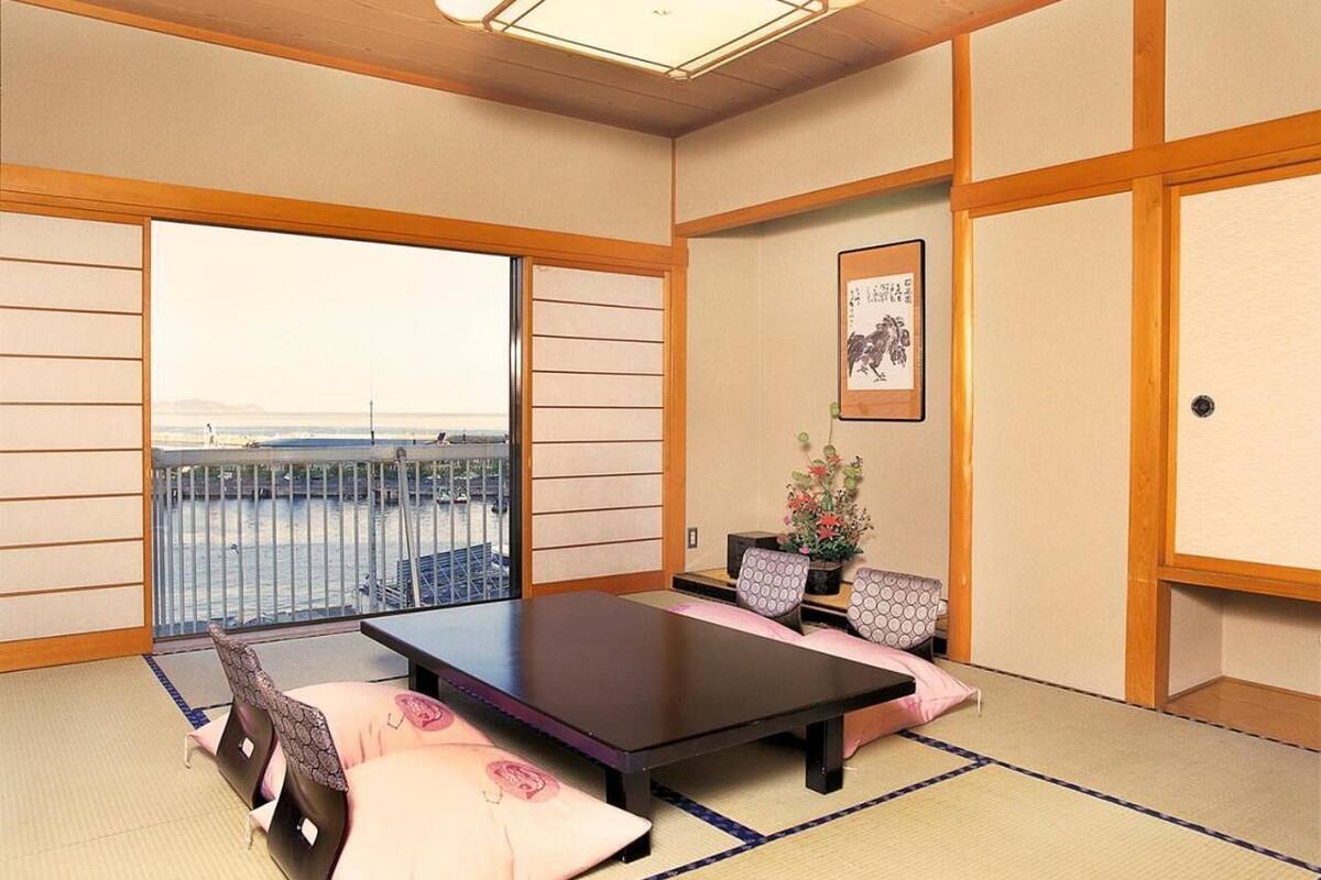 Una habitación japonesa tradicional con suelo de tatami, una mesa baja con cojines y vista al mar a través de amplios ventanales.