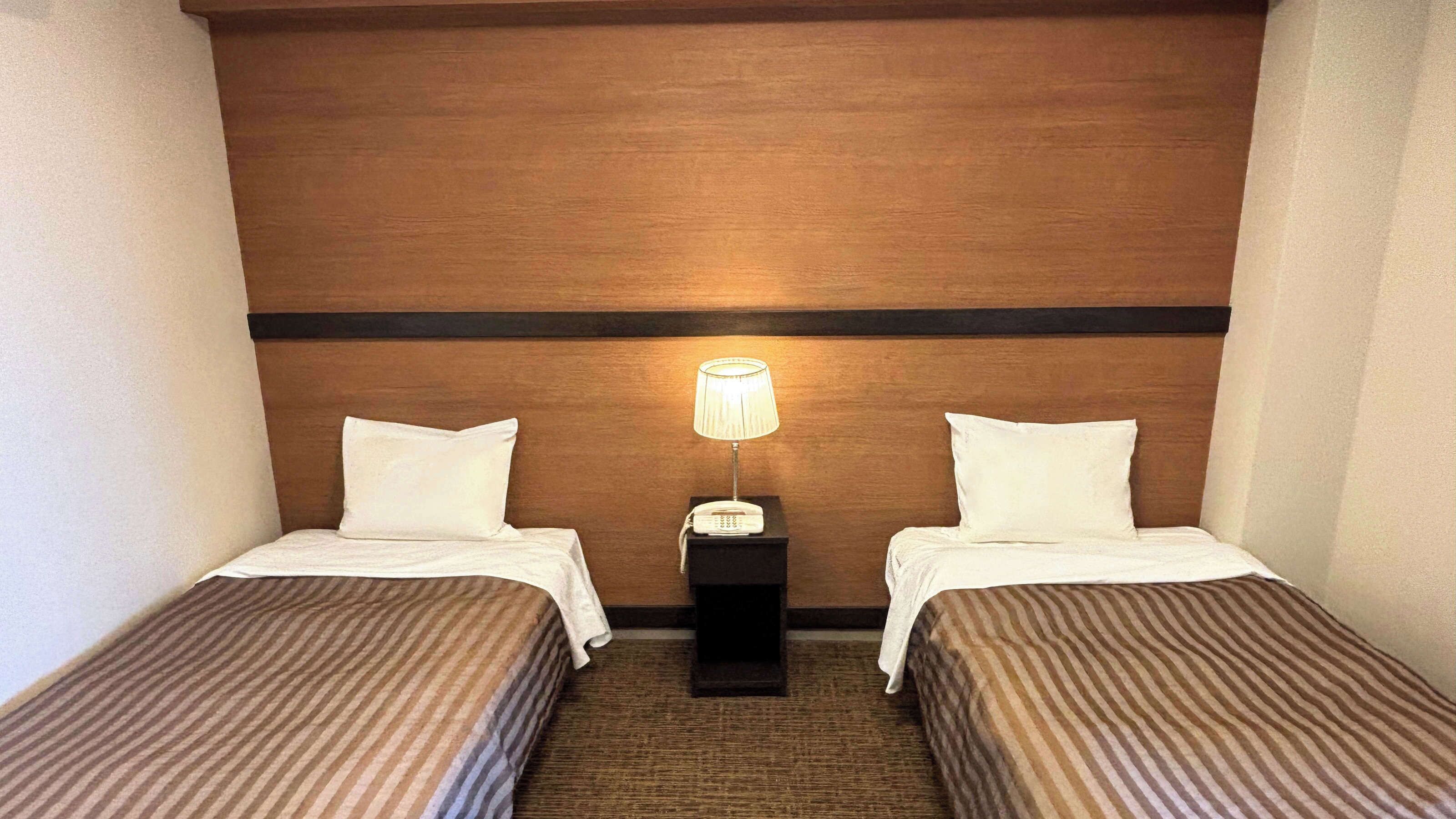 Una habitación de hotel con dos camas individuales, una mesita de noche con lámpara y cabecero de madera.